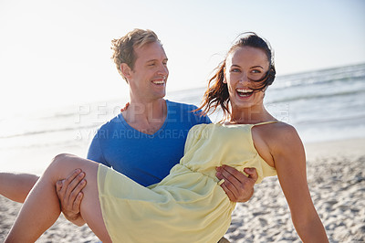 Buy stock photo Shot of a handsome man carrying his wife on the beach