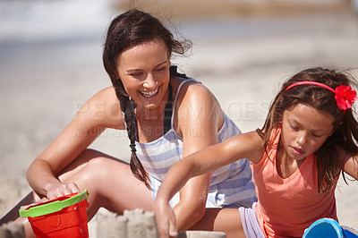 Buy stock photo Shot of a happy mother and daughter building sandcastles together at the beach