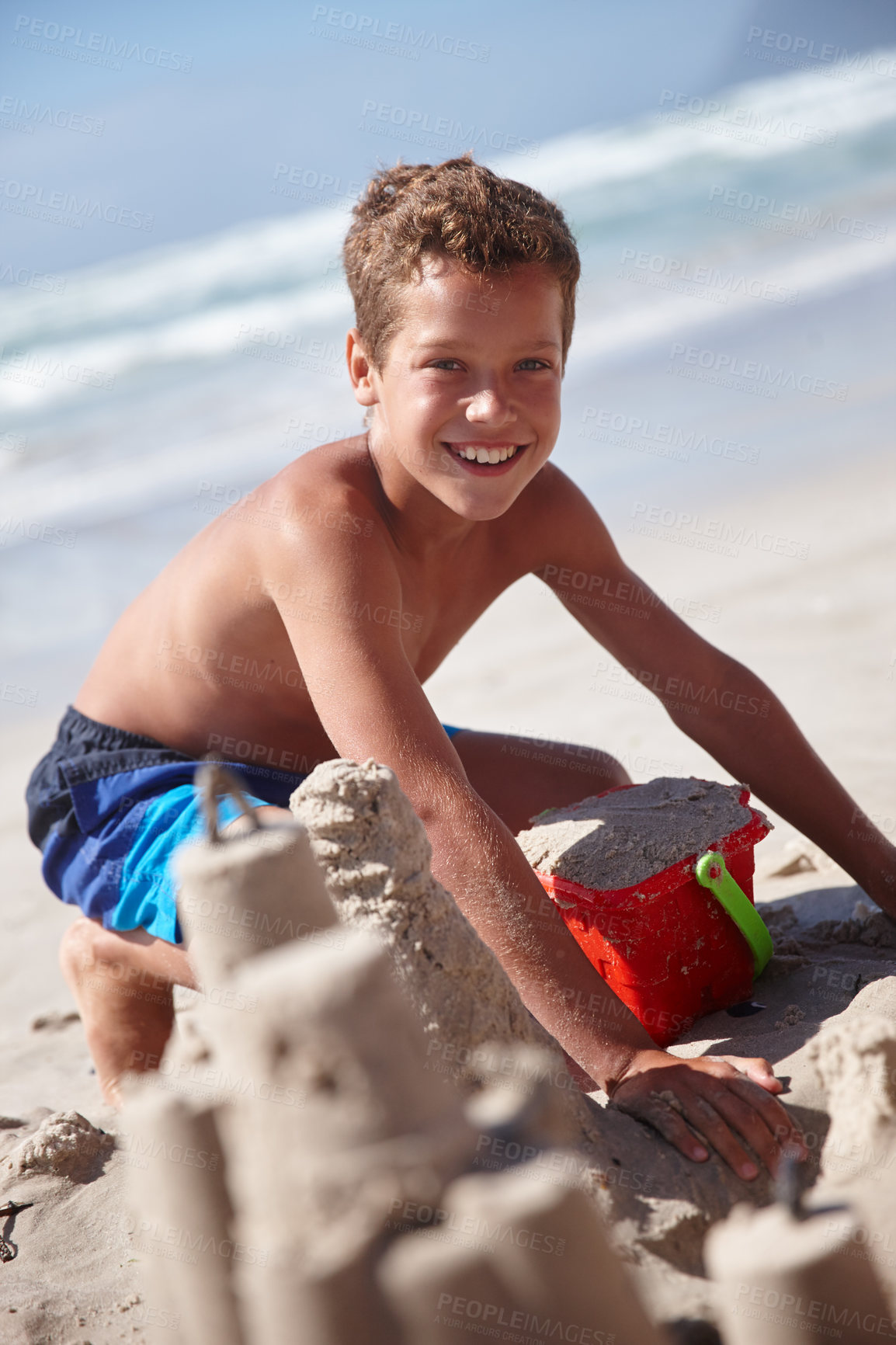 Buy stock photo Portrait, smile and kid with sandcastle at beach for travel, sand sculpting and holiday adventure. Happy, child and boy with bucket for playful fun, seaside activity and creative games on vacation