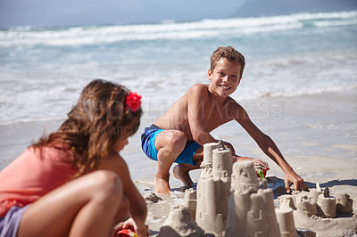 Buy stock photo Shot of a happy brother and sister building sandcastles together at the beach