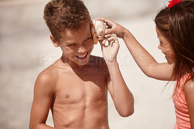 Buy stock photo Shot of a little girl holding a conch shell against her brother's ear