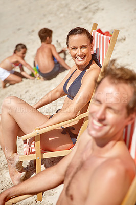Buy stock photo Shot of a couple sitting on beach chairs while their children play in the background