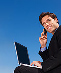 Executive using a laptop and cellphone against blue sky