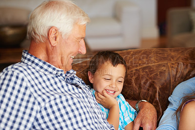 Buy stock photo Shot of a little boy sitting beside his grandfather on the sofa