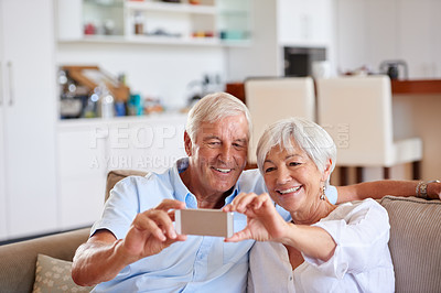 Buy stock photo Shot of a senior couple taking a selfie with their cellphone while sitting on the sofa