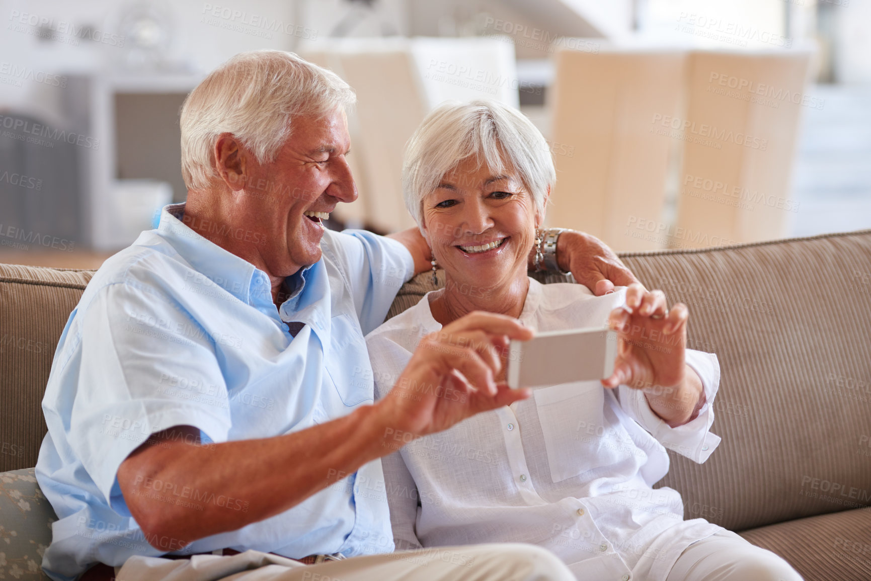 Buy stock photo Shot of a senior couple taking a selfie with their cellphone while sitting on the sofa