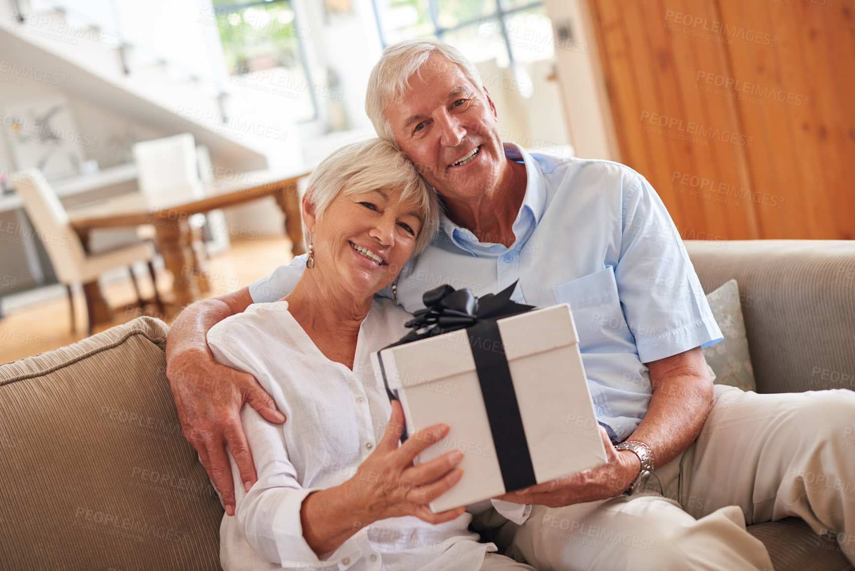 Buy stock photo Home, portrait and old couple on sofa, gift and bonding together with anniversary. Apartment, pensioner and mature woman on couch, man or present with love, relax or celebration with care or marriage