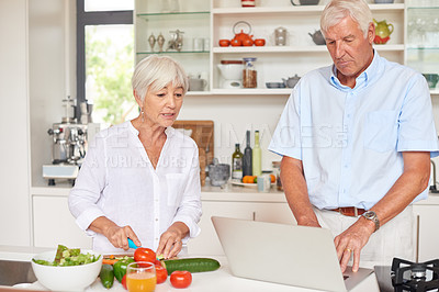 Buy stock photo Shot of a senior couple using a laptop while cooking