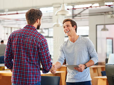 Buy stock photo Shot of two young businessmen shaking hands in a casual office