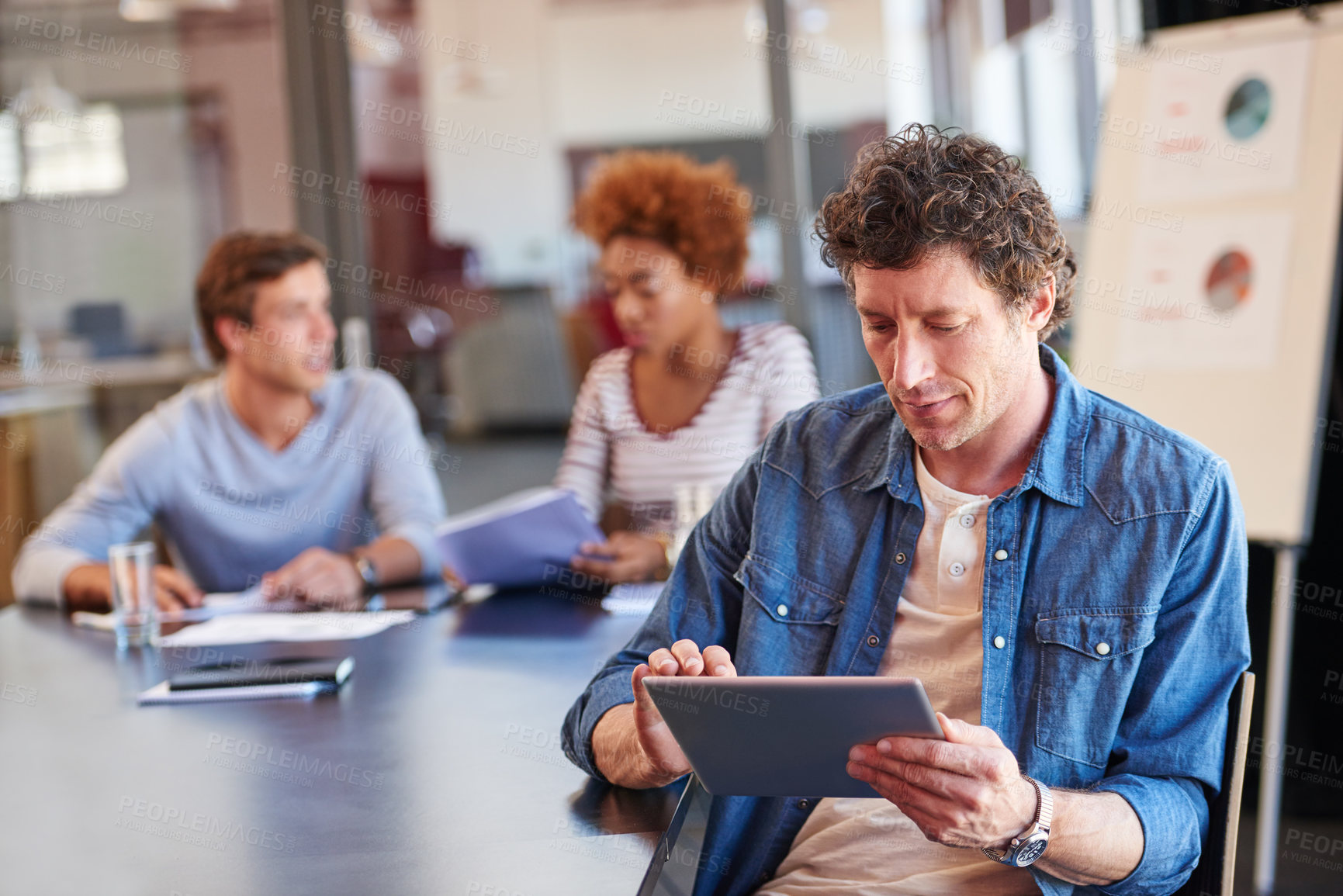 Buy stock photo Shot  of man using a digital tablet in a boardroom with his colleagues in the background