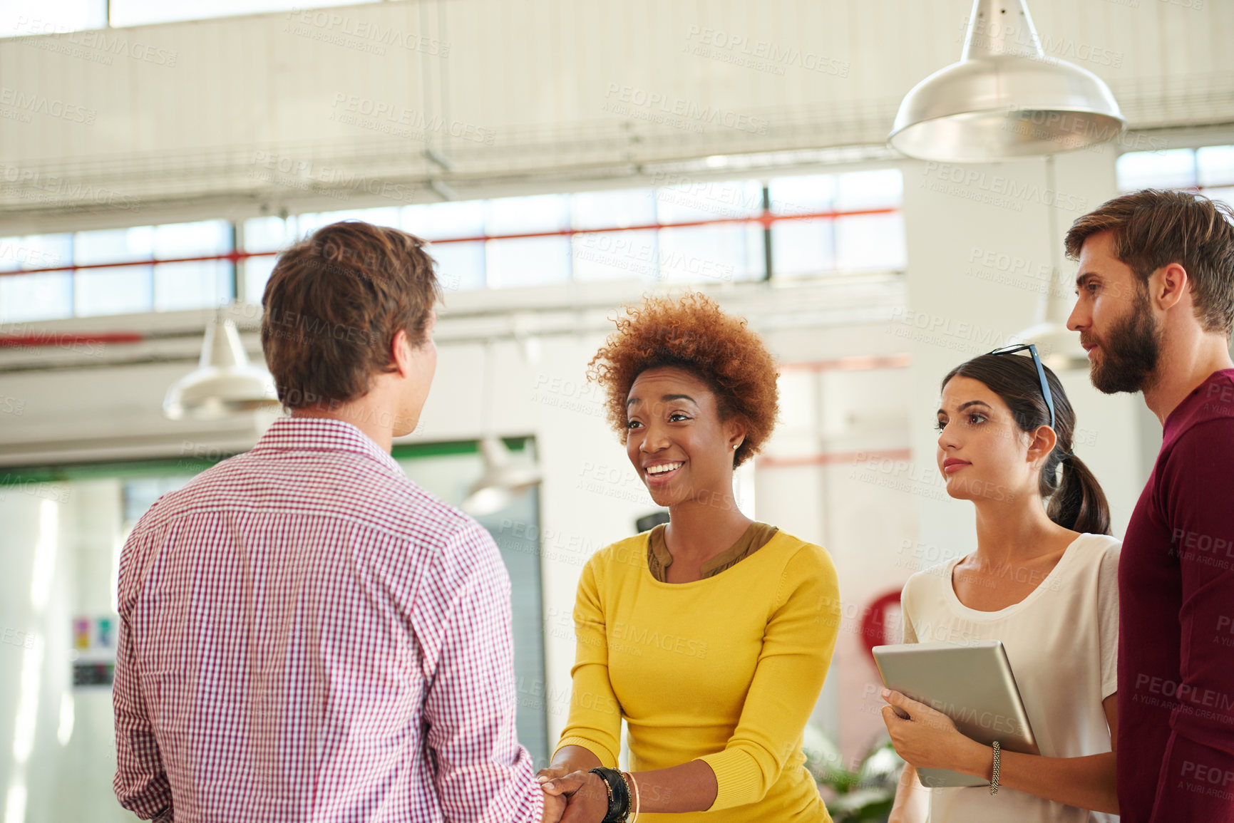 Buy stock photo Shot of two people shaking hands in an office while their coworkers look on