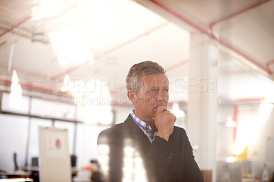 Buy stock photo Cropped through-the-window shot of a businessman standing in an office