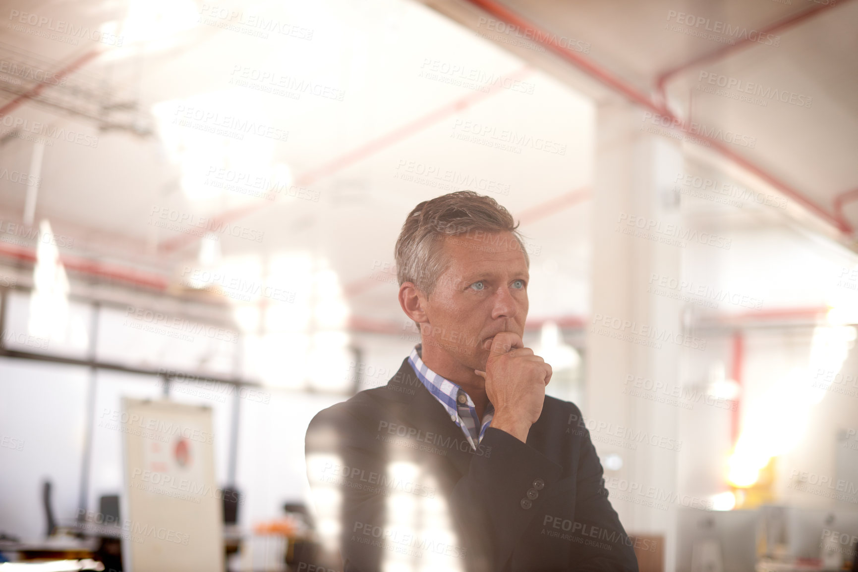 Buy stock photo Cropped through-the-window shot of a businessman standing in an office