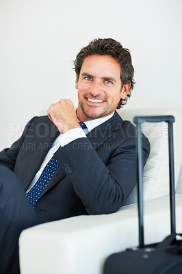 Buy stock photo Smiling middle aged executive sitting on a chair with travel suitcase