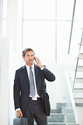Buy stock photo Handsome executive standing on the stairs with office bags and talking on cellphone