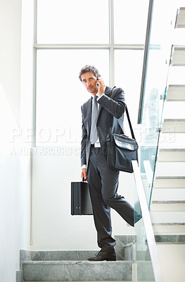 Buy stock photo Full length of smart mature executive using mobile phone and walking down the staircase with office bags