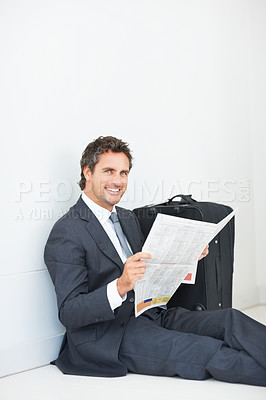 Buy stock photo Smart smiling business man sitting against wall reading newspaper and giving you a warm smile