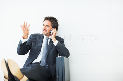 Buy stock photo Handsome executive sitting against wall and talking on cellphone
