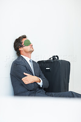 Buy stock photo Mature business man with a sleep mask sitting against wall with travel luggage