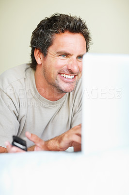 Buy stock photo Relax, phone and laptop with a man in the bedroom of his home for entertainment on weekend time off. Smile, tech and a happy man lying in bed, streaming a movie or series while internet browsing