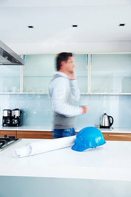 Buy stock photo Architect, phone call and busy man in conversation for planning building project, development and talkinh in kitchen. Engineer, blur and remote work for construction with helmet and blueprint in home