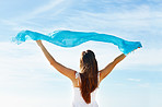 Young woman holding blue scarf against sky