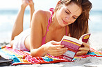 Beautiful young woman reading book on beach