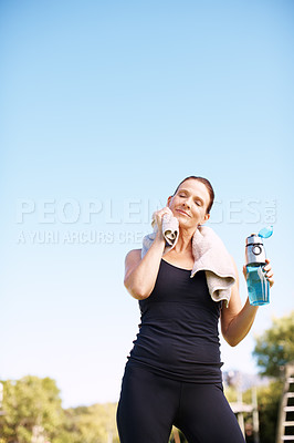 Buy stock photo A woman standing and rubbing her face with a towel after an outdoor workout