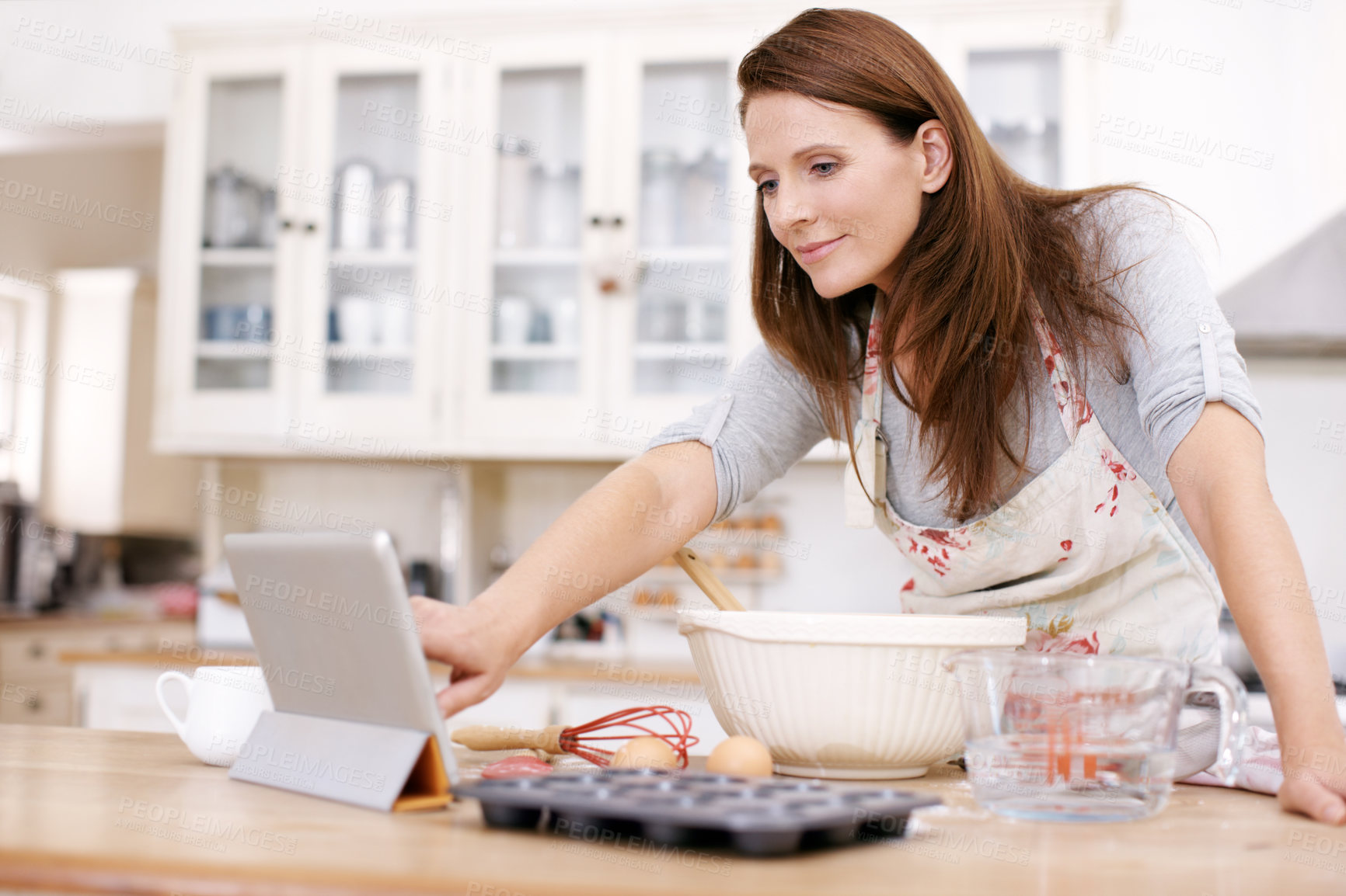 Buy stock photo Baking, woman and online with tablet at kitchen counter for ingredients, recipe or instructions on cake in home. Reading, browsing internet and baker person with bowl for dessert, cookies or cupcakes