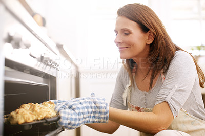 Buy stock photo A mature woman taking scones out from the oven
