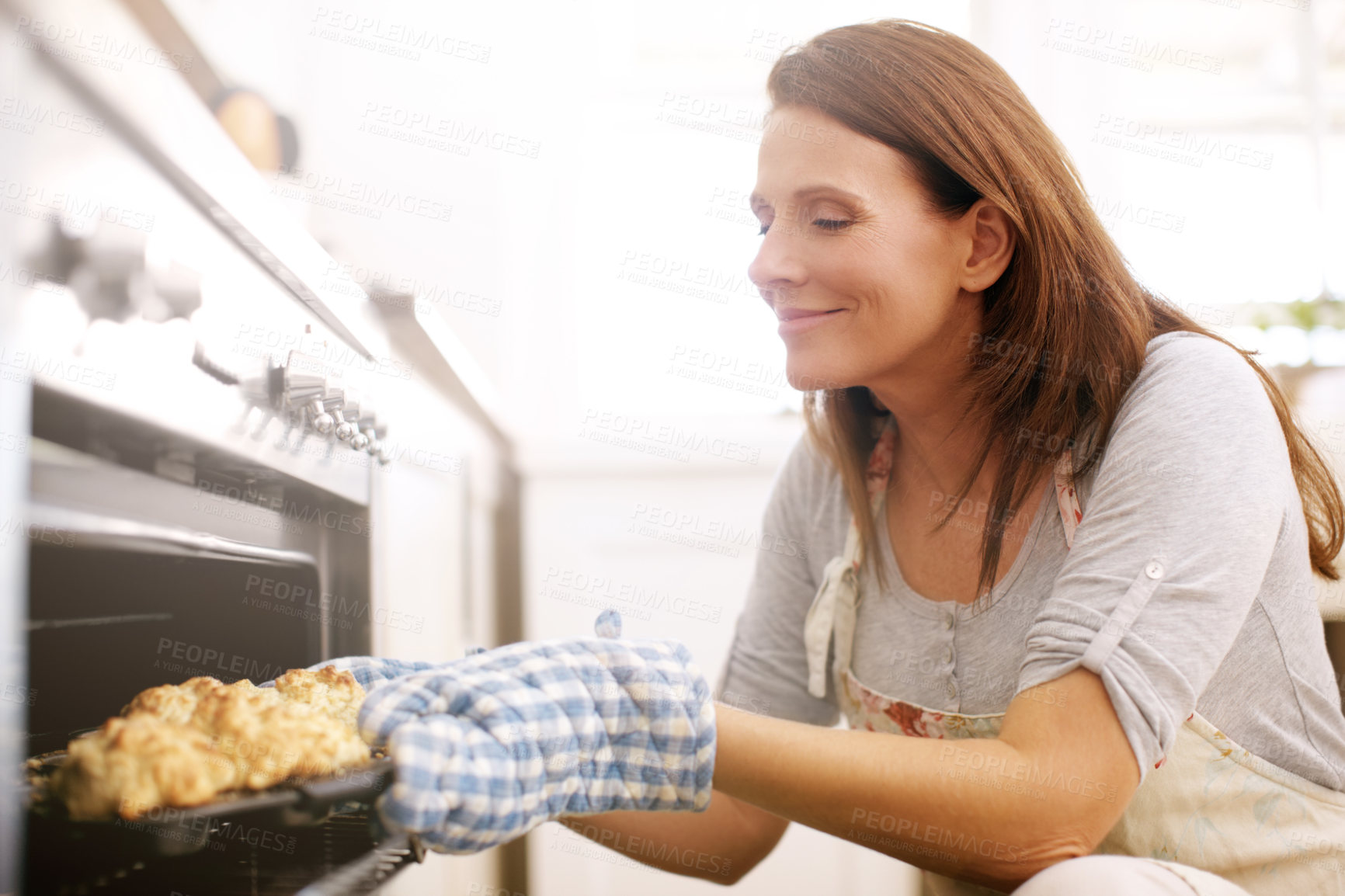 Buy stock photo A mature woman taking scones out from the oven