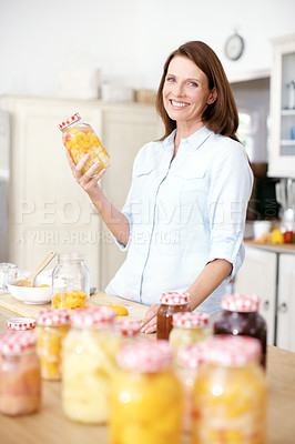 Buy stock photo A mature woman holding a jar of preserved fruit in the kitchen