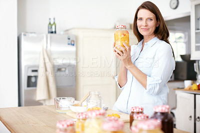 Buy stock photo A mature woman holding a jar of fruit in the kitchen