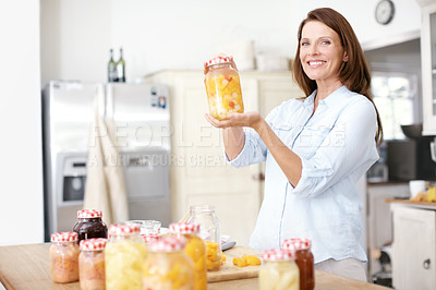 Buy stock photo A mature woman showing you her jar of peaches in the kitchen