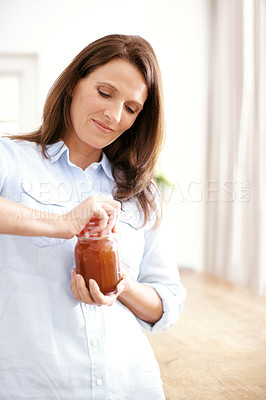 Buy stock photo A mature woman opening a jar in the kitchen