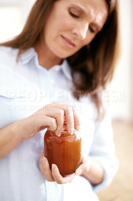Buy stock photo A mature woman struggling to open a jar in the kitchen