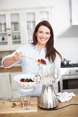 Buy stock photo An attractive woman adding fruit to a blender while standing at a kitchen counter