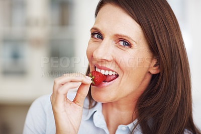 Buy stock photo Closeup shot of an attractive brunette eating a strawberry while standing in a kitchen