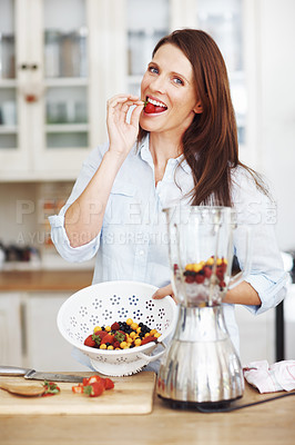 Buy stock photo An attractive brunette eating a strawberry while preparing a smoothie