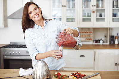 Buy stock photo An attractive woman pouring blended fruit into a glass while standing at a kitchen counter