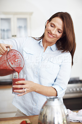 Buy stock photo An attractive woman pouring blended fruit into a glass while standing at a kitchen counter