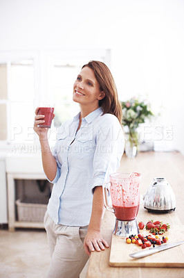 Buy stock photo An attractive woman enjoying a fruit smoothie while leaning against a kitchen counter