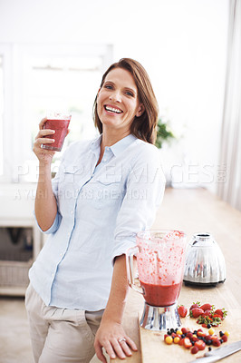 Buy stock photo An attractive woman enjoying a fruit smoothie while leaning against a kitchen counter