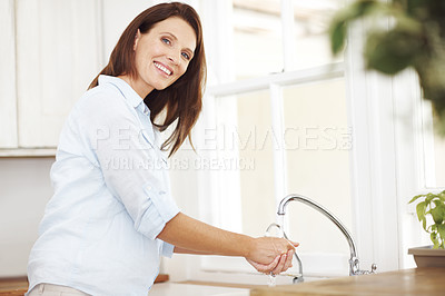 Buy stock photo An attractive woman washing her hands by the kitchen sink