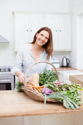 Buy stock photo A beautiful woman in her kitchen with a basket full of fresh vegetables