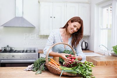 Buy stock photo A beautiful woman stands in her kitchen while inspecting the vegetables in a basket on her counter.
