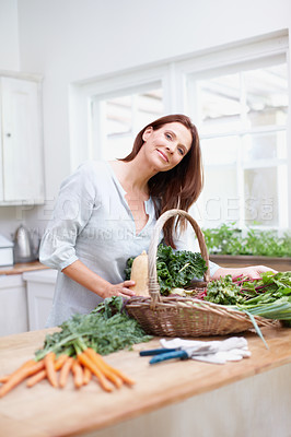 Buy stock photo Portrait of a beautiful woman standing behind her kitchen counter with a basket of fresh vegetables