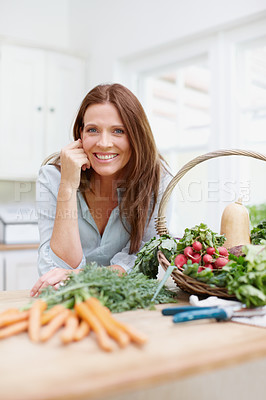 Buy stock photo A beautiful woman leans on her kitchen counter behing a basket of fresh  vegetables