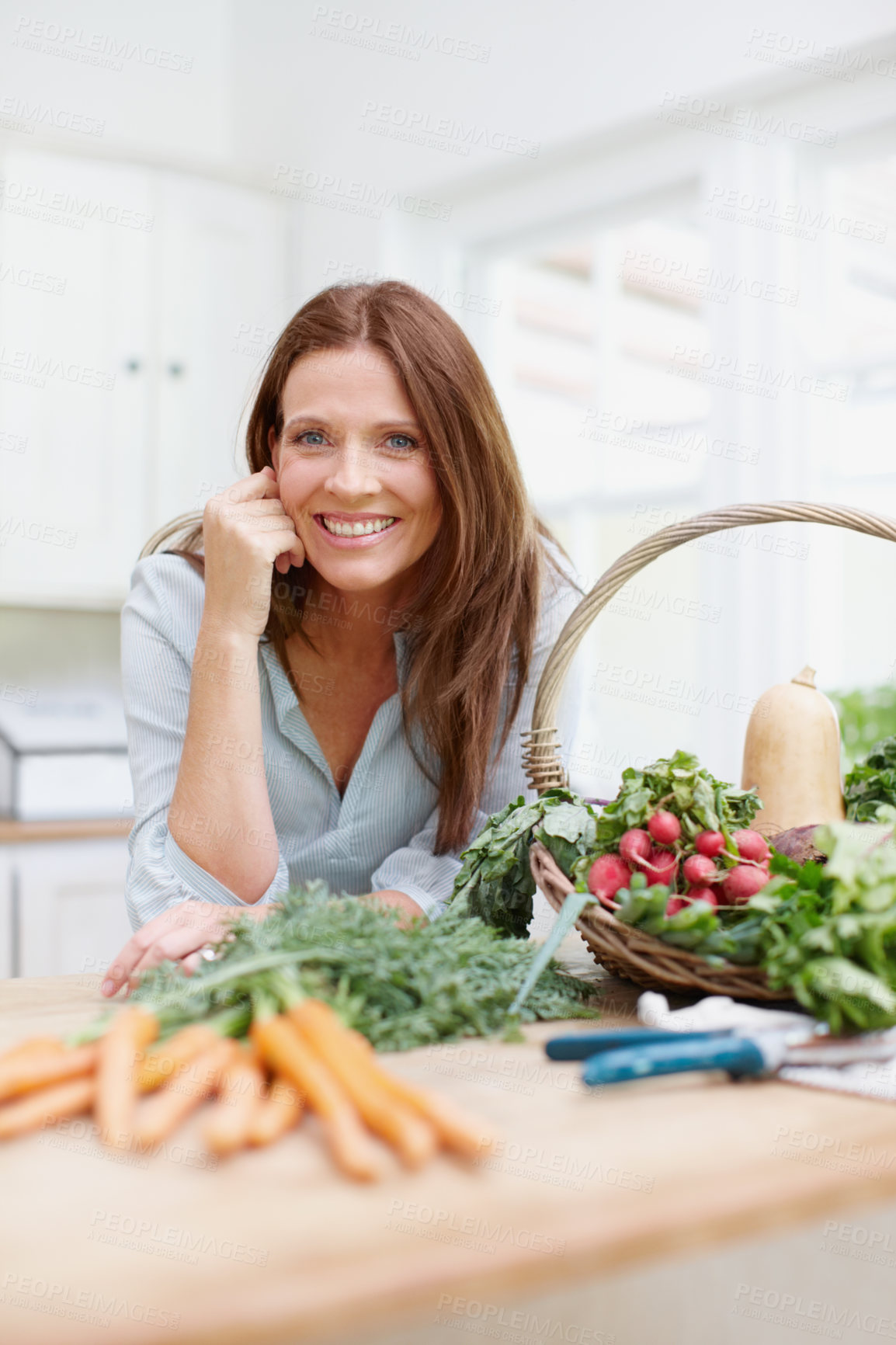 Buy stock photo A beautiful woman leans on her kitchen counter behing a basket of fresh  vegetables