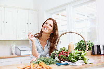 Buy stock photo A beautiful woman looks up to the left while leaning on her kitchen counter next to a basket full of vegetables